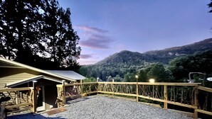 A covered outdoor area with a gravel floor, wooden deck, and a view of a forested hillside. - Best View in Bat Cave (Hendersonville)