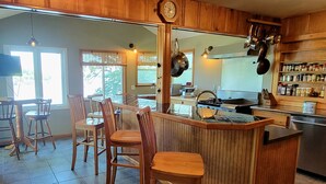 A kitchen with wooden cabinets, a central island with stools, a dining area with chairs, and a large window. - Dog Friendly and Beautiful Main Channel View at the 34.5MM in a "NO WAKE" cove.. (Sunrise Beach)
