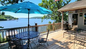 A wooden deck with a table and chairs, a blue umbrella, and an American flag. - Dog Friendly and Beautiful Main Channel View at the 34.5MM in a "NO WAKE" cove.. (Sunrise Beach)