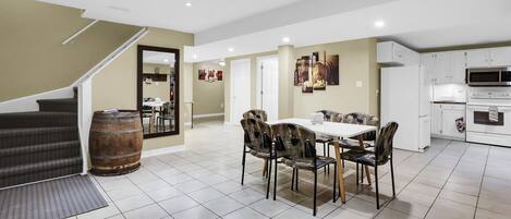 Uma sala de estar ampla, com uma mesa de jantar, cadeiras e uma cozinha equipada com eletrodomésticos modernos.