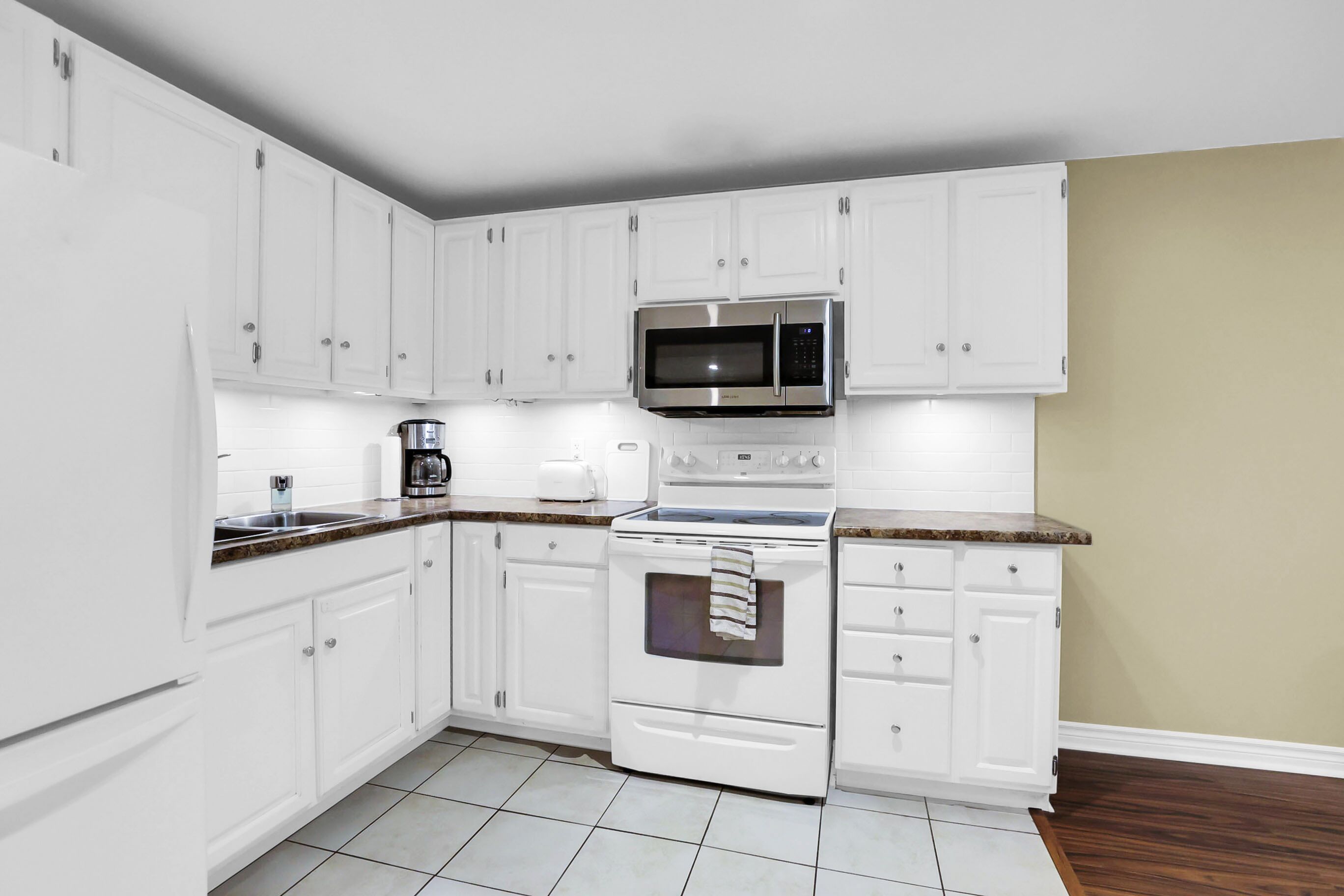 A kitchen with white cabinets, a microwave, a stove, and a coffee maker.