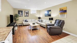 A modern living room with a sofa, armchair, coffee table, and a flat-screen TV. - Niagara Falls Retreat: Walk to the Wonders (Niagara Falls)