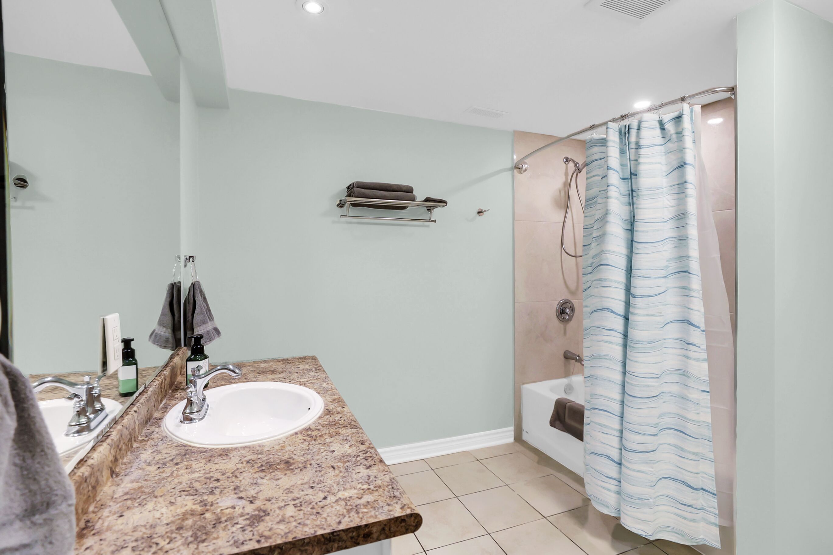 A bathroom with a granite countertop sink, a towel rack, a shower curtain, and a bathtub.