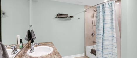 A bathroom with a granite countertop sink, a towel rack, a shower curtain, and a bathtub.