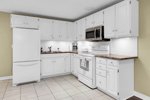 Una cocina moderna con armarios blancos, un microondas de acero inoxidable, una cafetera y una estufa.