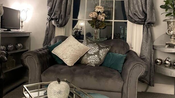 A living room with a dark brown sofa, a glass coffee table, and a chandelier. - 5 Bed House - Sleeps 12 - Pets - Parking (Ross-on-Wye)
