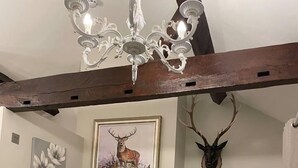 A bedroom with a wooden ceiling, a chandelier, a bed with a deer pillow, a framed deer painting, a deer antler, and a nightstand with a lamp. - 5 Bed House - Sleeps 12 - Pets - Parking (Ross-on-Wye)