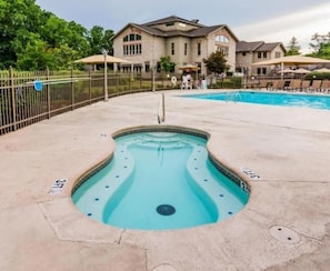 A swimming pool with a unique shape, surrounded by a fence, with a building in the background.