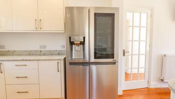 Una cocina con un refrigerador de acero inoxidable, un dispensador de agua, armarios blancos y piso de madera.