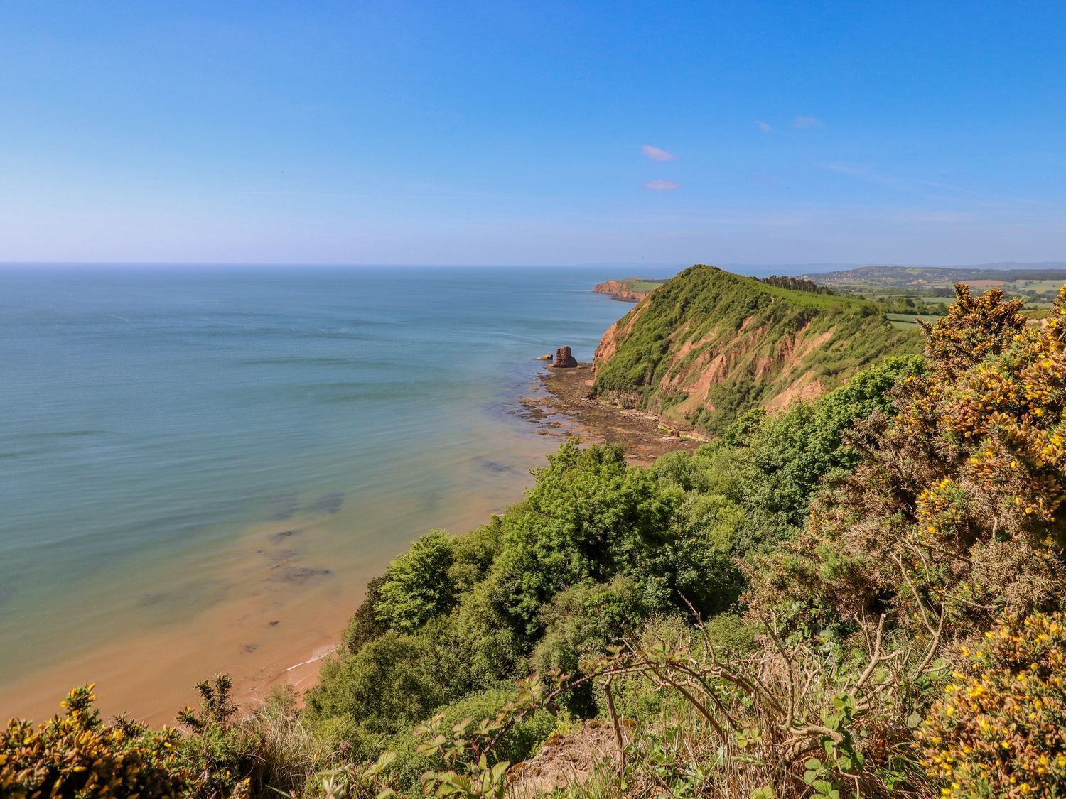 Un paisaje costero con vista despejada al mar, una playa de arena y una ladera verde.