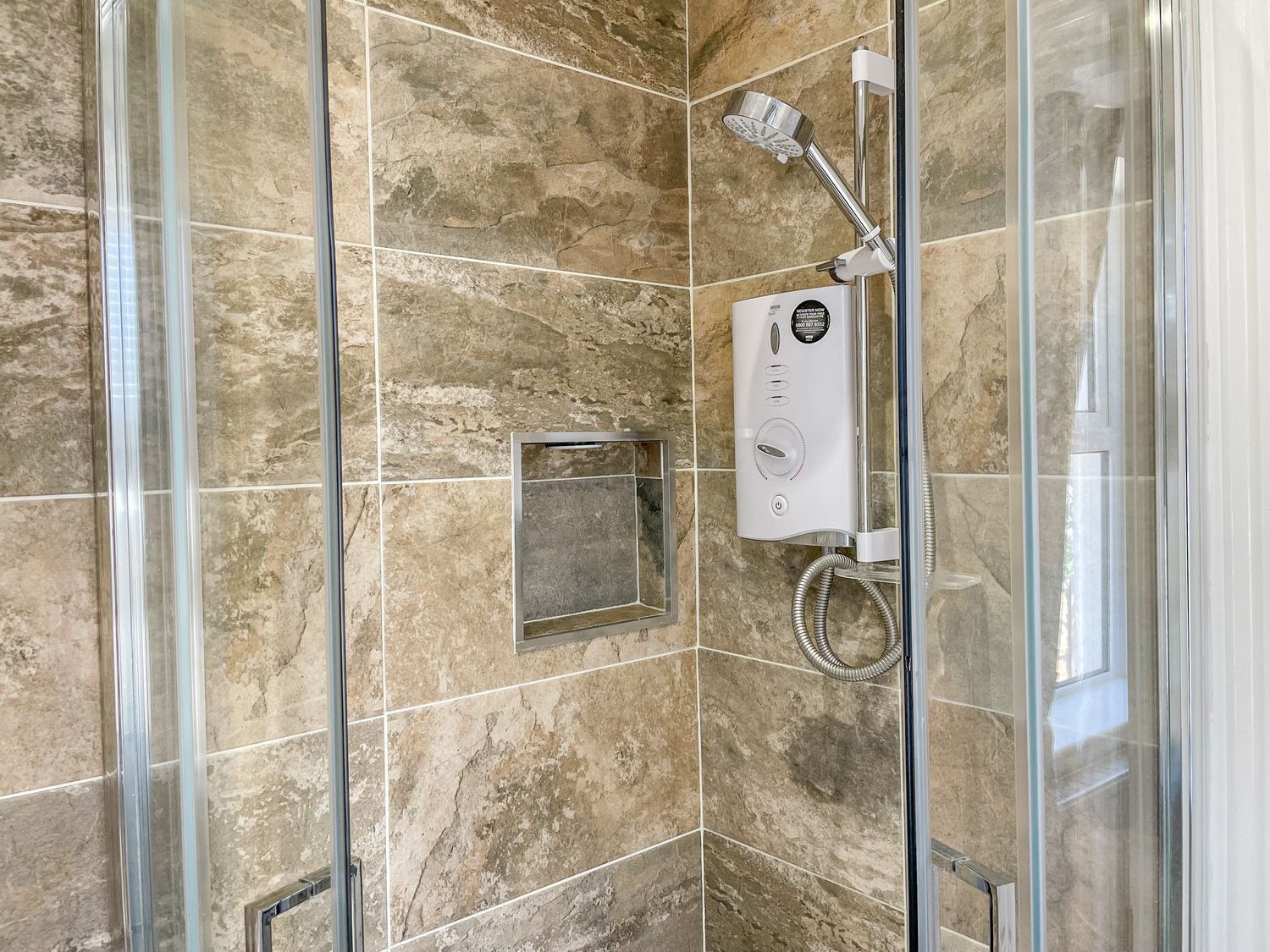 Ducha con cerramiento de vidrio, cabezal de ducha manual y panel de control.