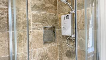 Ducha con cerramiento de vidrio, cabezal de ducha manual y panel de control.