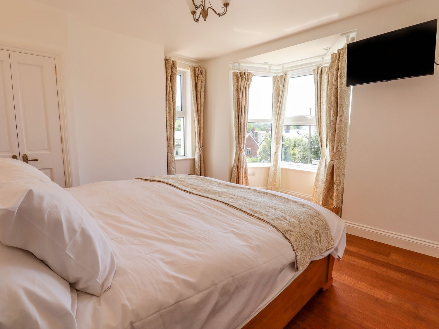 Une chambre avec un grand lit, un téléviseur fixé au mur et une fenêtre avec des rideaux.