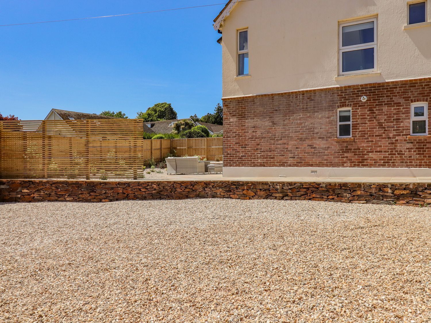 A residential building with a brick facade, a stone retaining wall, and a gravel driveway.