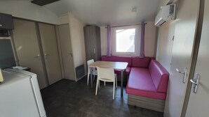 Une petite cuisine équipée comprenant un réfrigérateur, une petite table avec des chaises et un canapé rose.