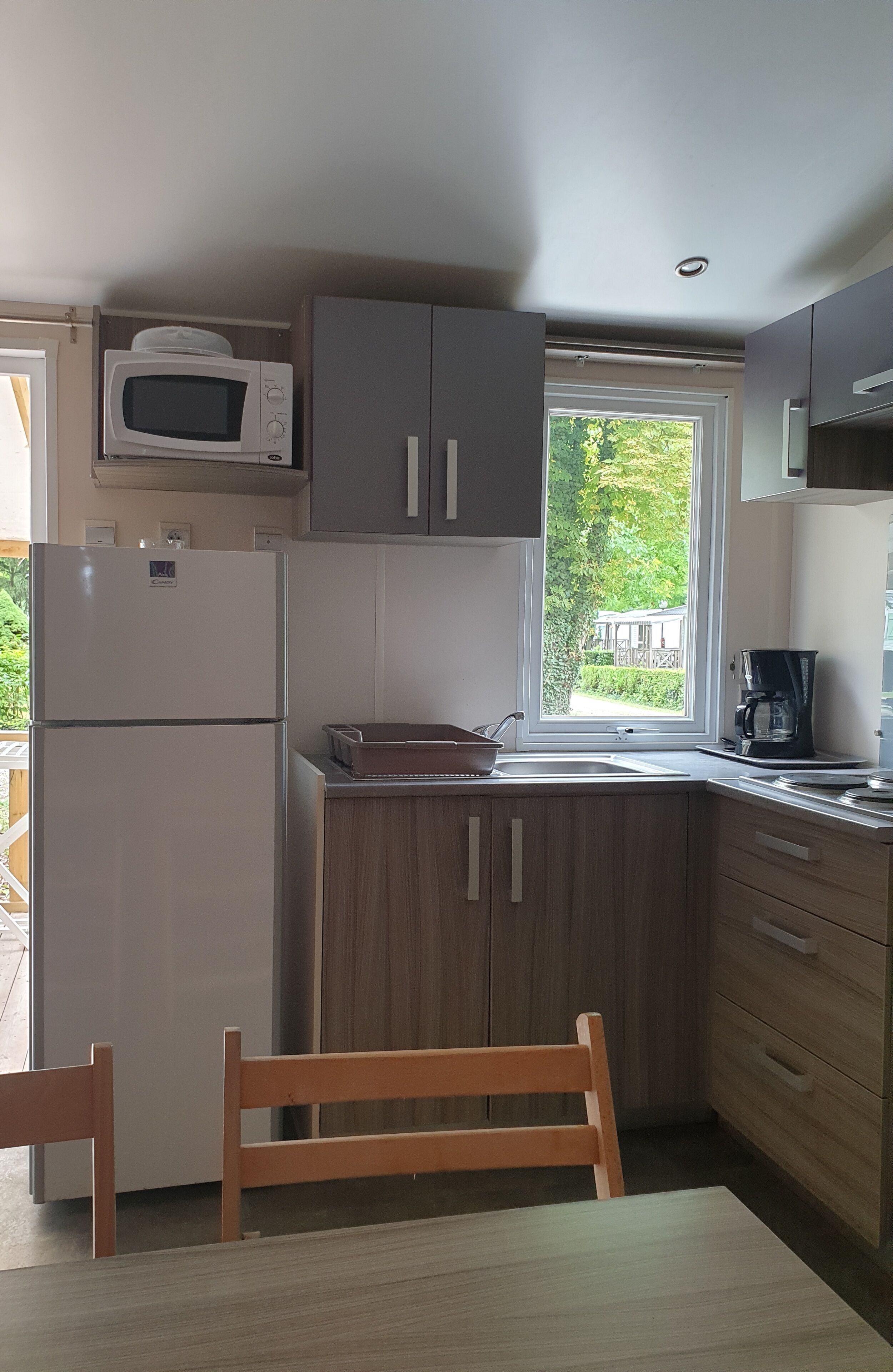A compact kitchen with a refrigerator, microwave, and a coffee maker. There's a window providing a view of greenery outside.