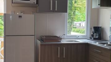 A compact kitchen with a refrigerator, microwave, and a coffee maker. There's a window providing a view of greenery outside.
