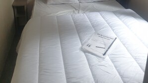 Un lit bien fait, avec une literie blanche, une tête de lit et une table de chevet sur laquelle se trouve une lampe.