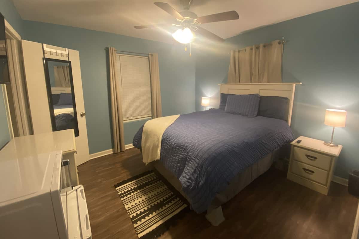 A bedroom with a bed, bedside tables, a ceiling fan, and a window with curtains.