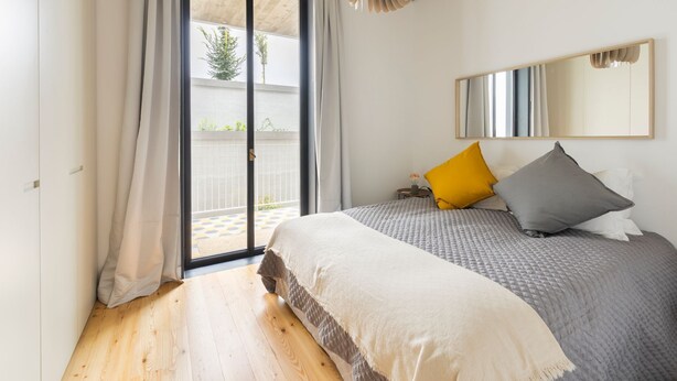 Une chambre à coucher avec un lit, une fenêtre avec des rideaux, un miroir et une vue sur l’extérieur.