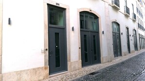 Une rangée de bâtiments avec des portes numérotées, une rue pavée et une façade de couleur claire.