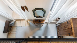 Une pièce aux hauts plafonds, ornée d’un grand miroir octogonal au centre, d’une table en bois sur laquelle sont disposées des bougies, et d’un radiateur en dessous.