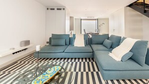 Un salon moderne avec un canapé d’angle, une table basse en verre et un skateboard.