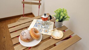 Een houten tafel met een bord donuts, een koffiezetapparaat, een kleine potplant en een zeeschelp.