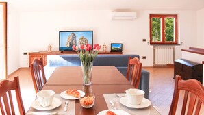A dining area with a wooden table set for two, a vase with flowers, and a television displaying a scenic image. - Arya's House - wi fi, air conditioning, sea view, parking (Campania)