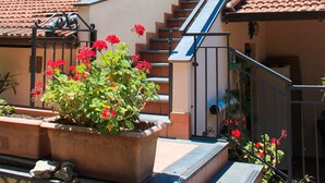 A two-story building with a tiled roof, a staircase, and a garden with red flowers. - Arya's House - wi fi, air conditioning, sea view, parking (Campania)