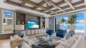 A spacious living room with a large flat-screen TV, comfortable seating, and a view of the ocean.