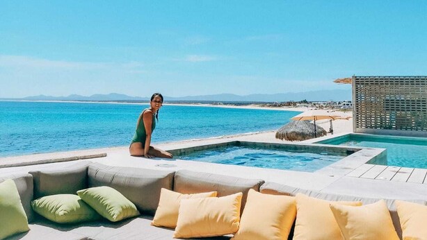 Un área de piscina con vista al océano, un espacio de descanso con cojines y una estructura de techo de paja.