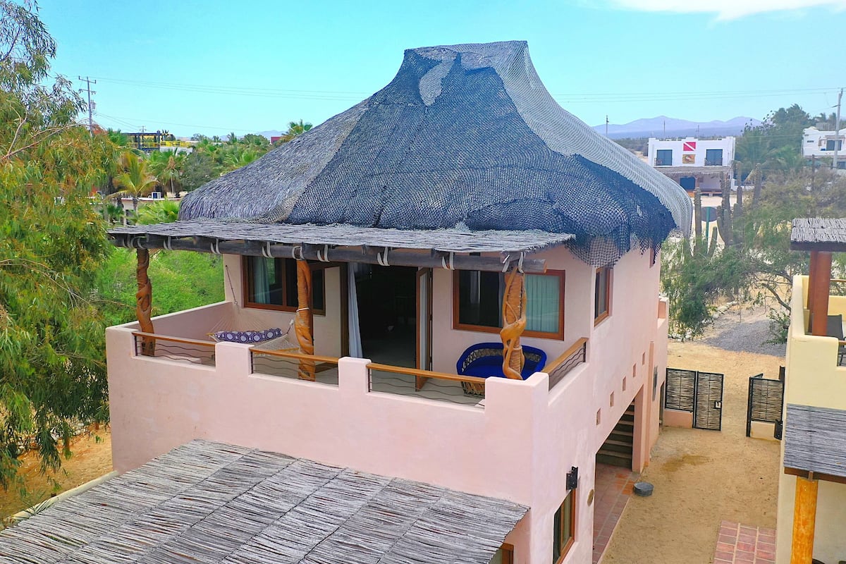 Una casa de dos pisos con techo de paja, un balcón y vistas del paisaje circundante.