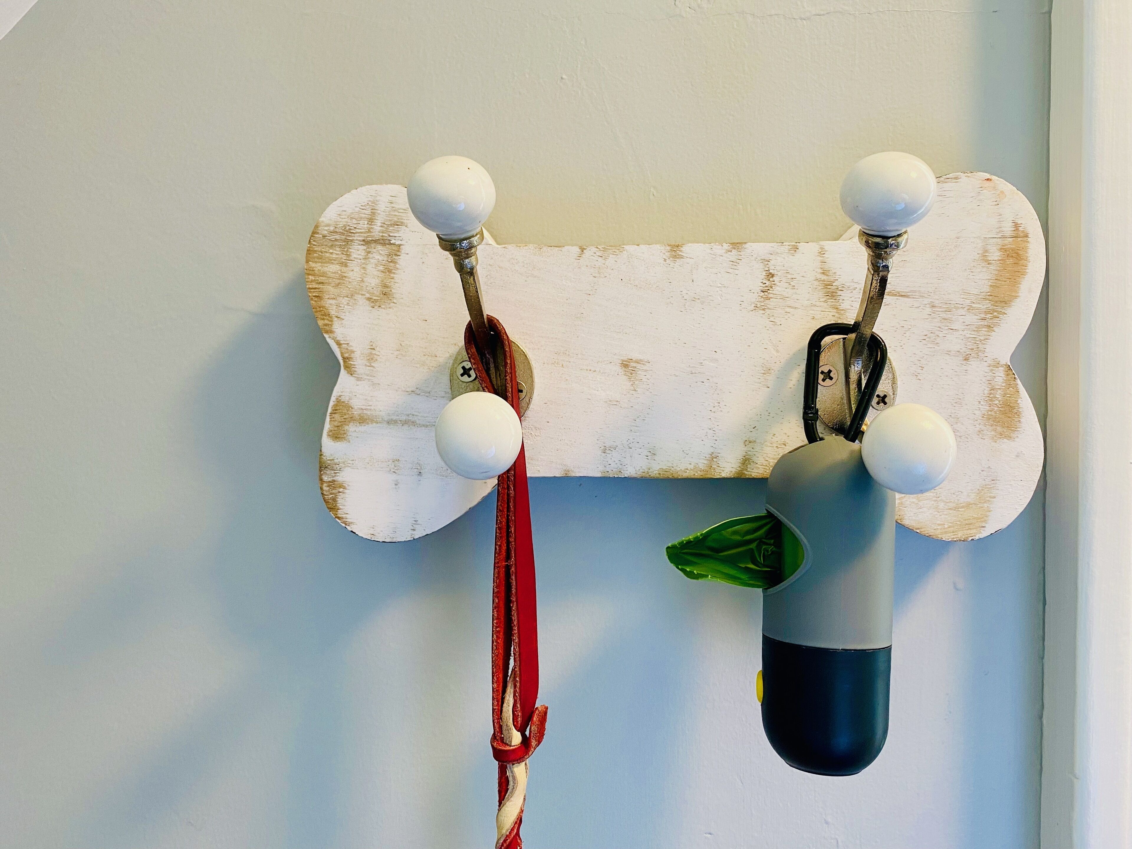 A wall-mounted coat rack with a rustic, distressed design, featuring a bone-shaped backrest and multiple hooks for hanging items.