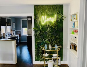 Una cocina con pared verde, un letrero de neón y un carrito de servicio dorado.