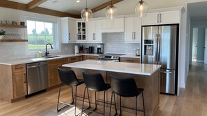 A modern kitchen with white cabinets, stainless steel appliances, and a central island with bar stools. - Lady Bug Lane Escape, Clinton, PEI (Clinton)