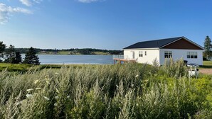 A white house with a dark roof, a dock, and a lake in the background. - Lady Bug Lane Escape, Clinton, PEI (Clinton)