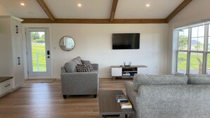 A spacious living room with a grey sofa, a coffee table, and a TV mounted on the wall. - Lady Bug Lane Escape, Clinton, PEI (Clinton)
