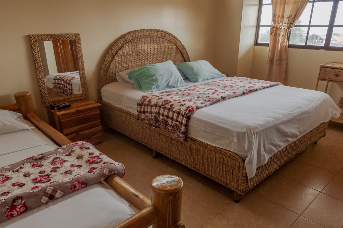 A bedroom with two beds, a wicker headboard, a nightstand, and a mirror.