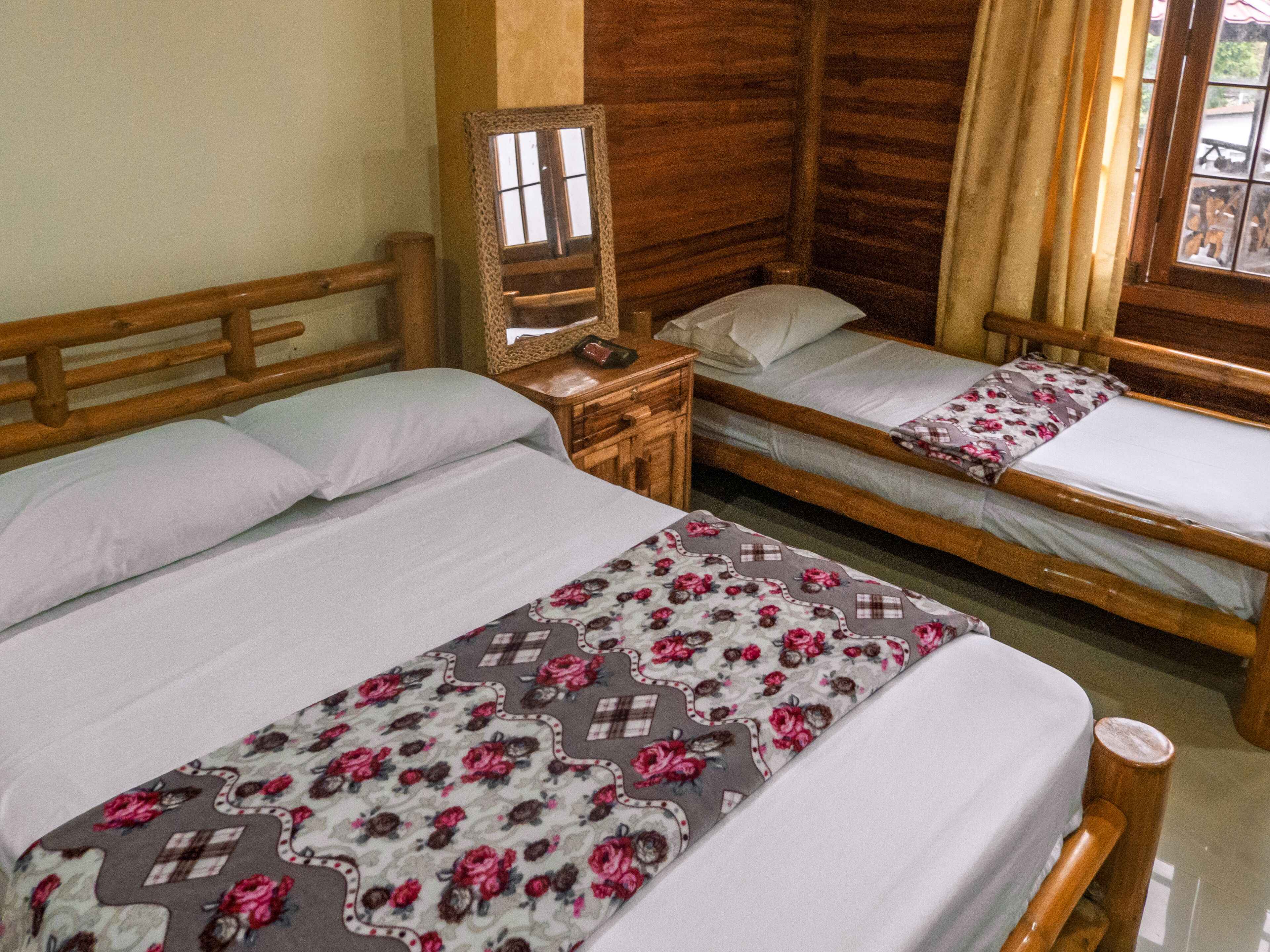 A room with two wooden beds, a nightstand, and a mirror.