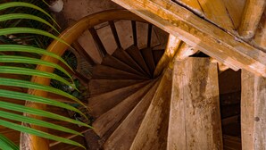 A wooden spiral staircase with a natural, rustic design, surrounded by greenery. - Hostal Poseidon (Puerto Cayo)