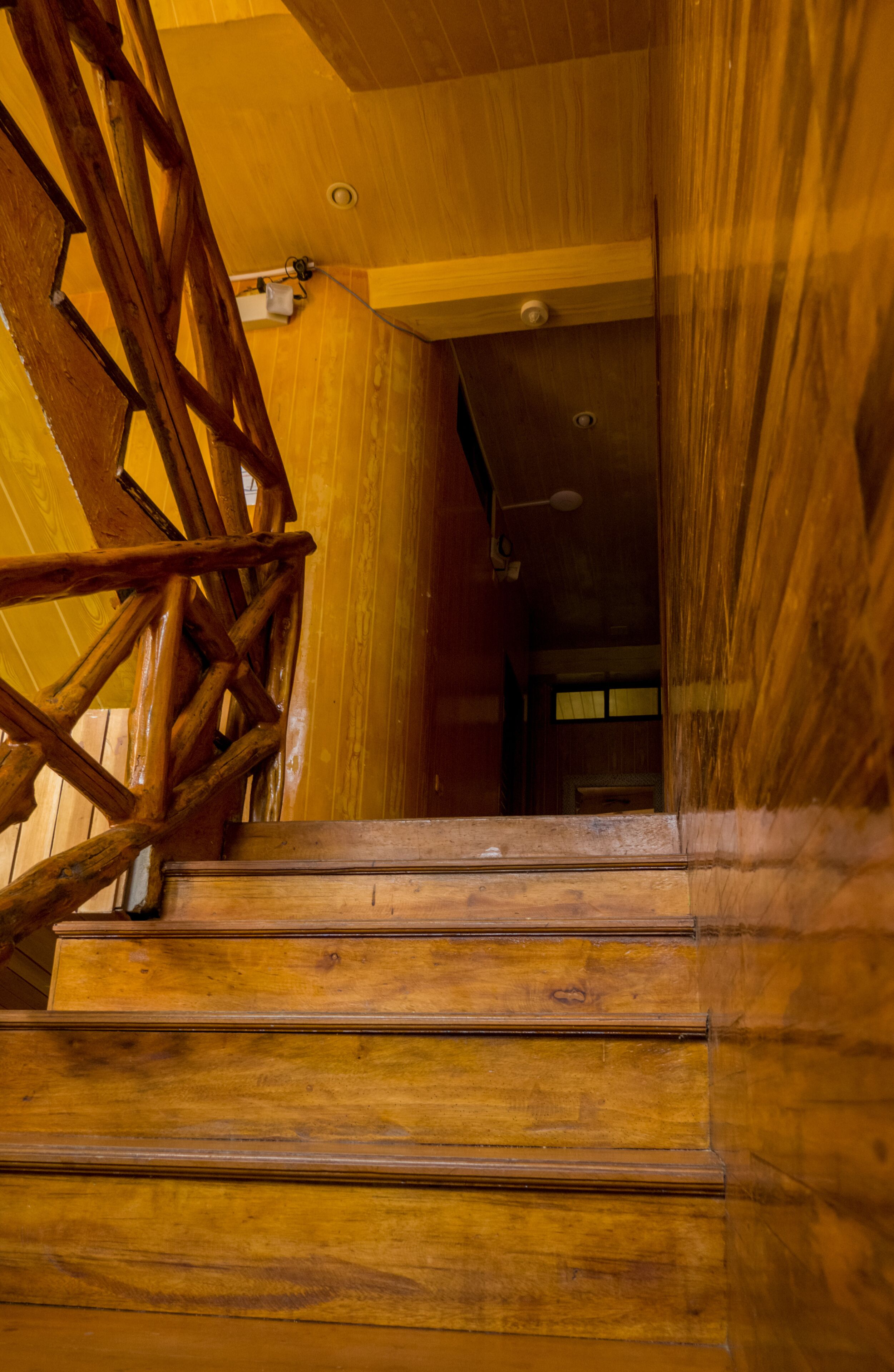 Una escalera de madera con barandilla que lleva a una habitación con techo y paredes de madera.
