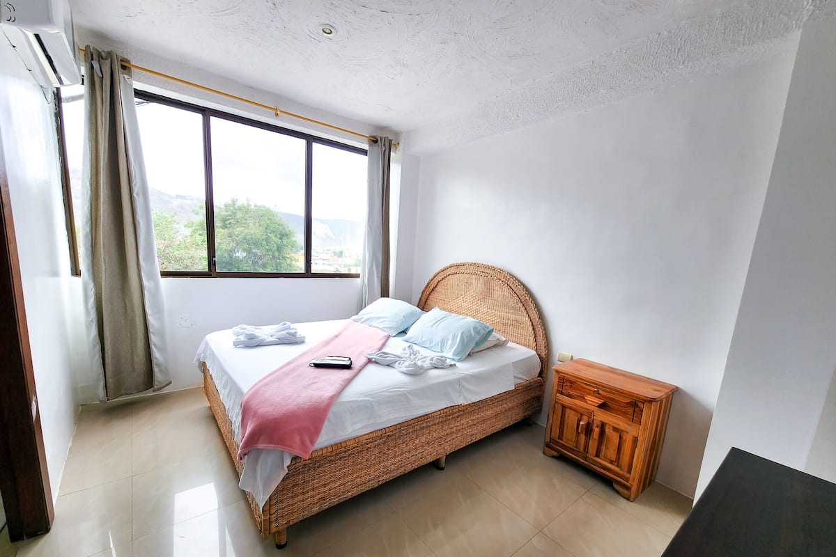 A bedroom with a wicker bed, a wooden nightstand, and a window with curtains.