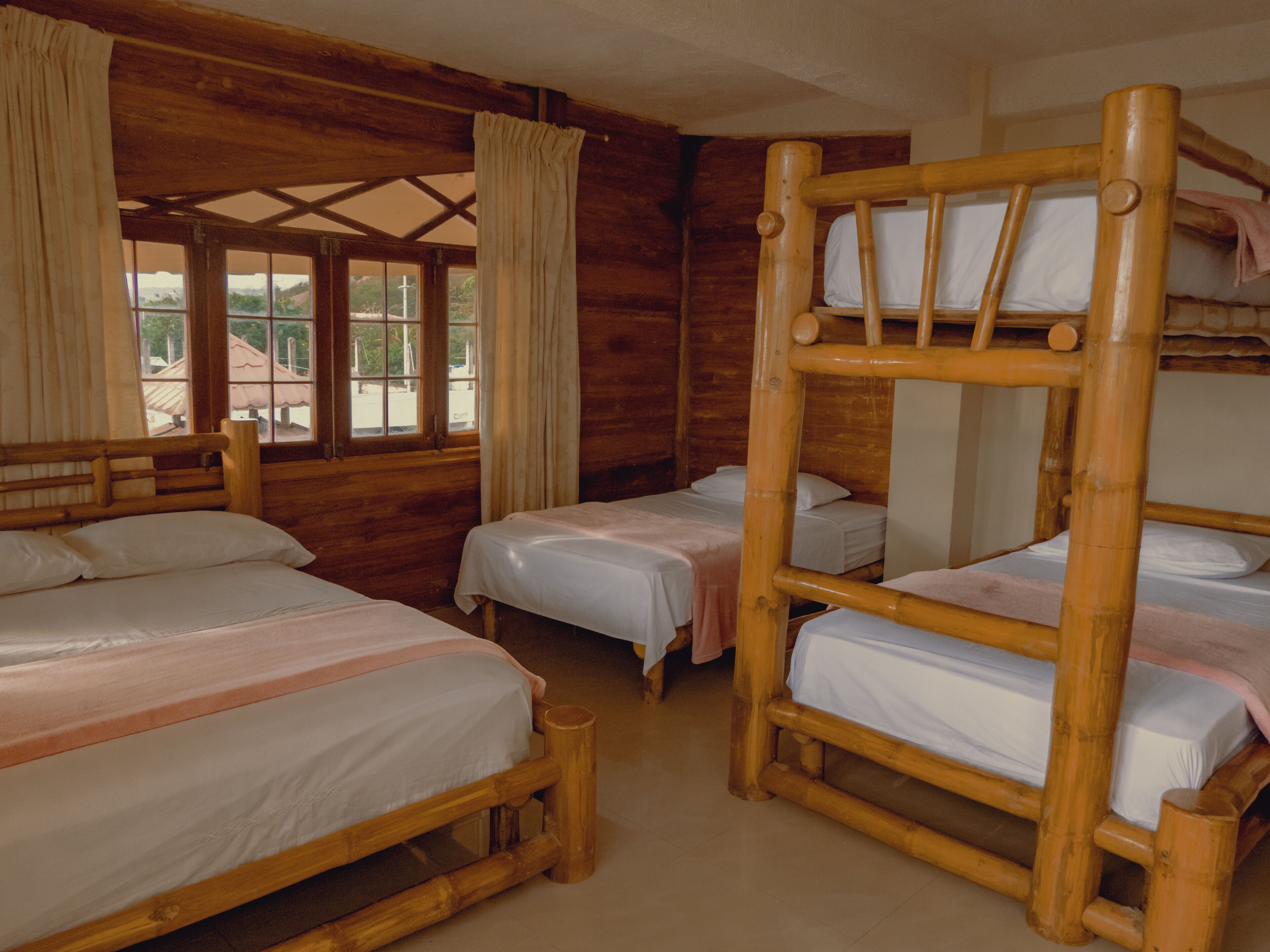 A cabin with three wooden bunk beds, a wooden headboard, and a window with curtains.