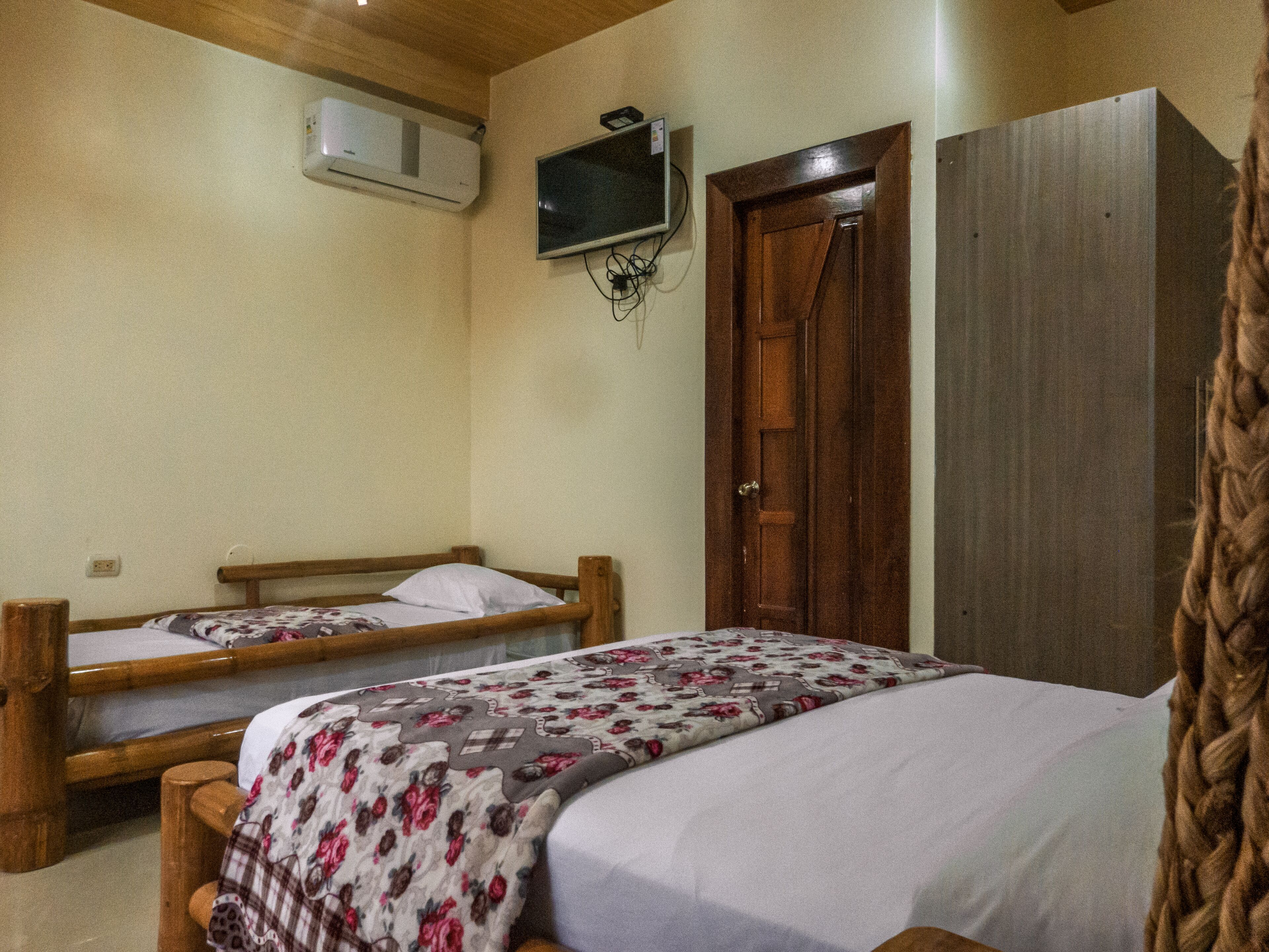Un dormitorio con dos camas de madera, un armario de madera, un televisor montado en la pared y un equipo de aire acondicionado.
