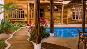 A wooden cabin with a covered patio, a pool, and a winding wooden pathway. - Hostal Poseidon (Puerto Cayo)