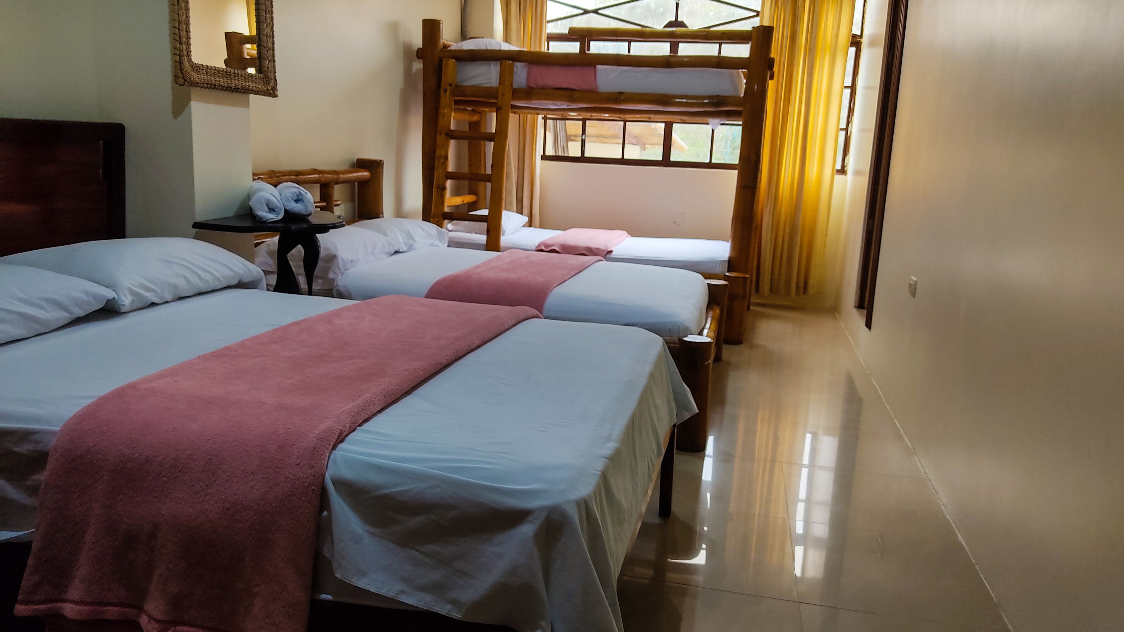 A hotel room with bunk beds, a wooden ladder, a small table with a chair, and a mirror on the wall.