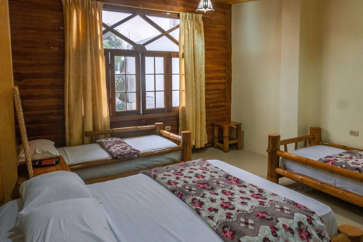 A room with two wooden beds, a small wooden stool, a wooden bench, and a window with curtains.