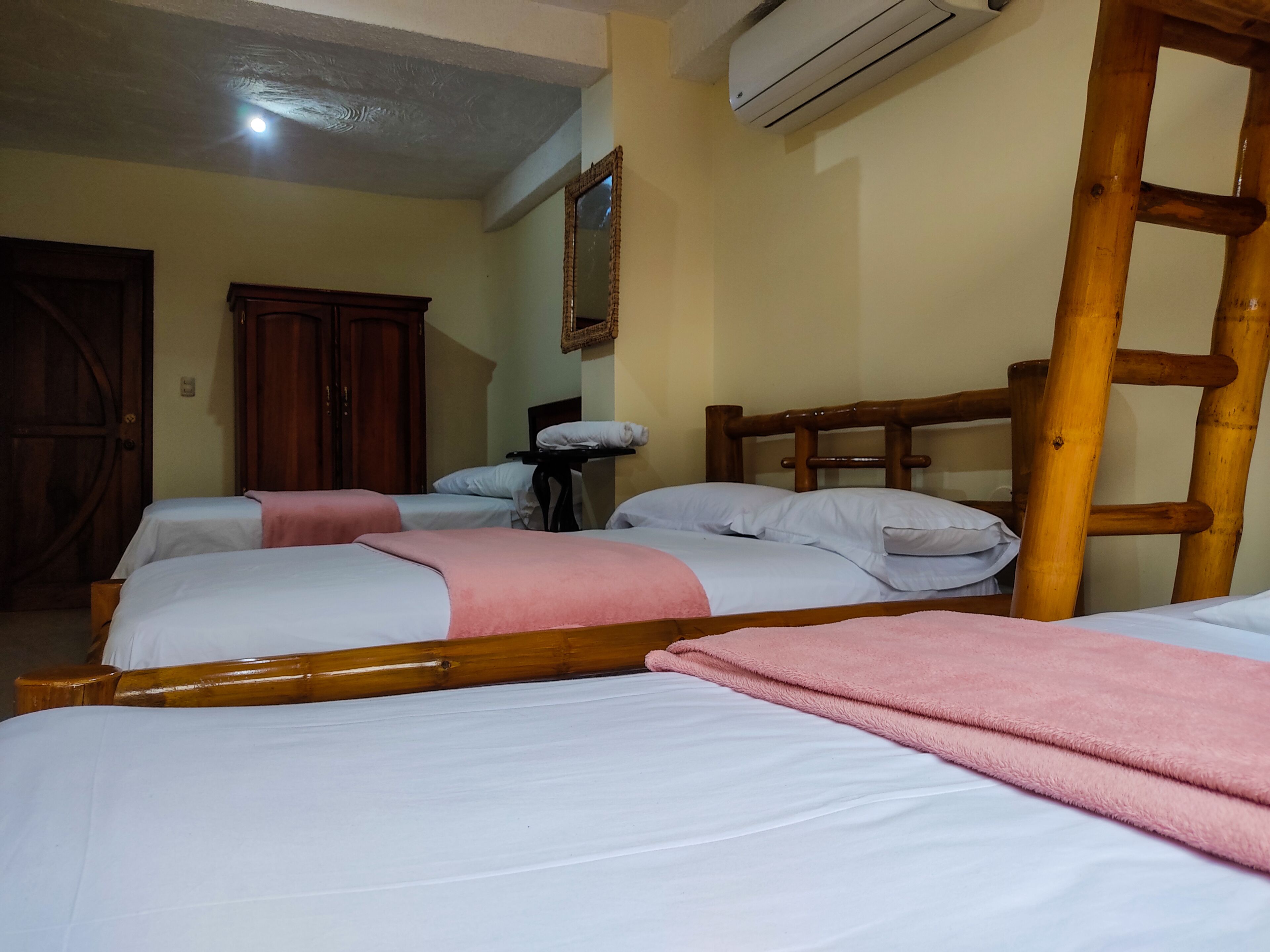 A room with two beds, a wooden ladder, an air conditioning unit, and a wooden wardrobe.