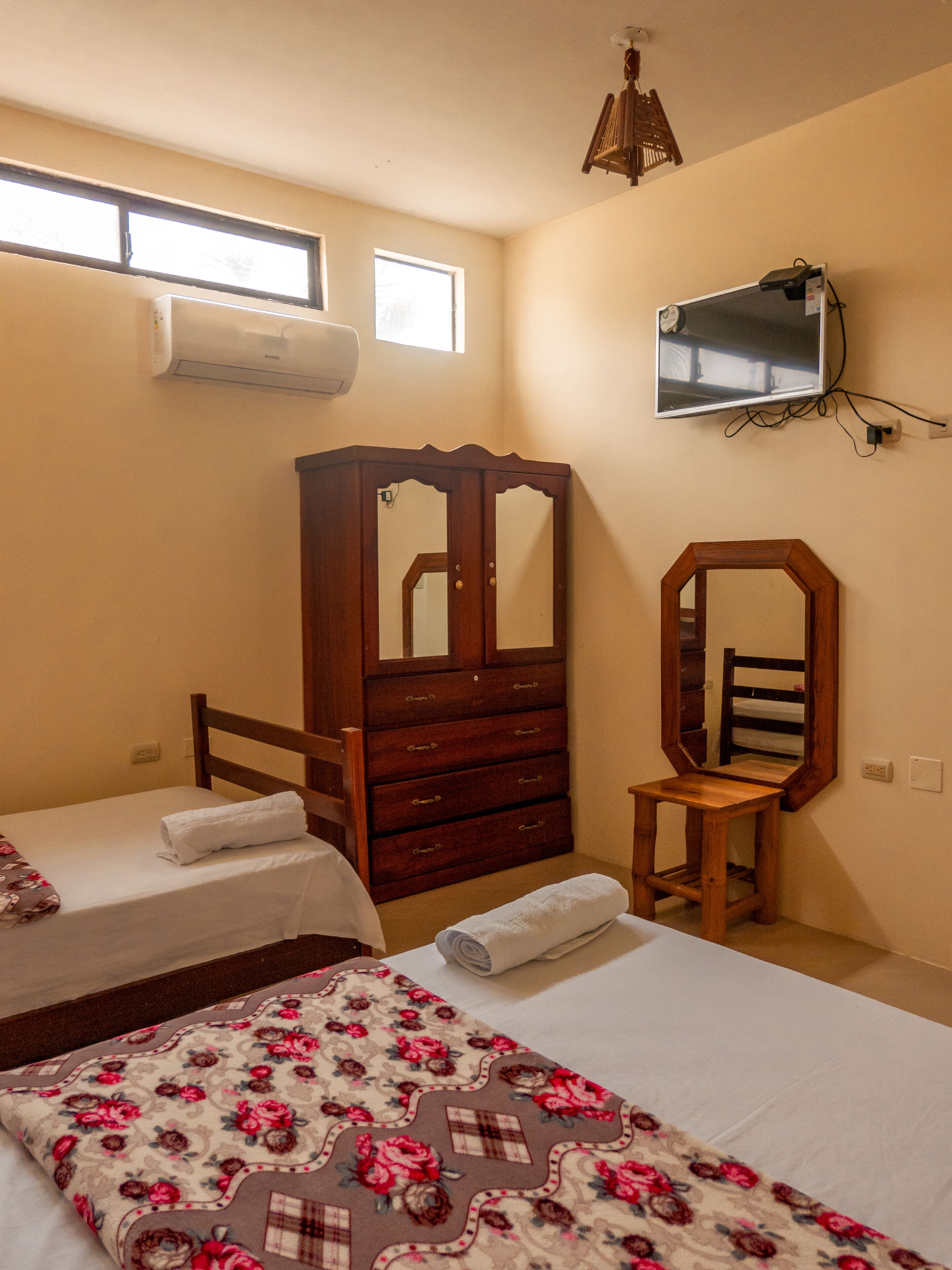 Une chambre avec deux lits, une commode en bois, un miroir et un téléviseur fixé au mur.